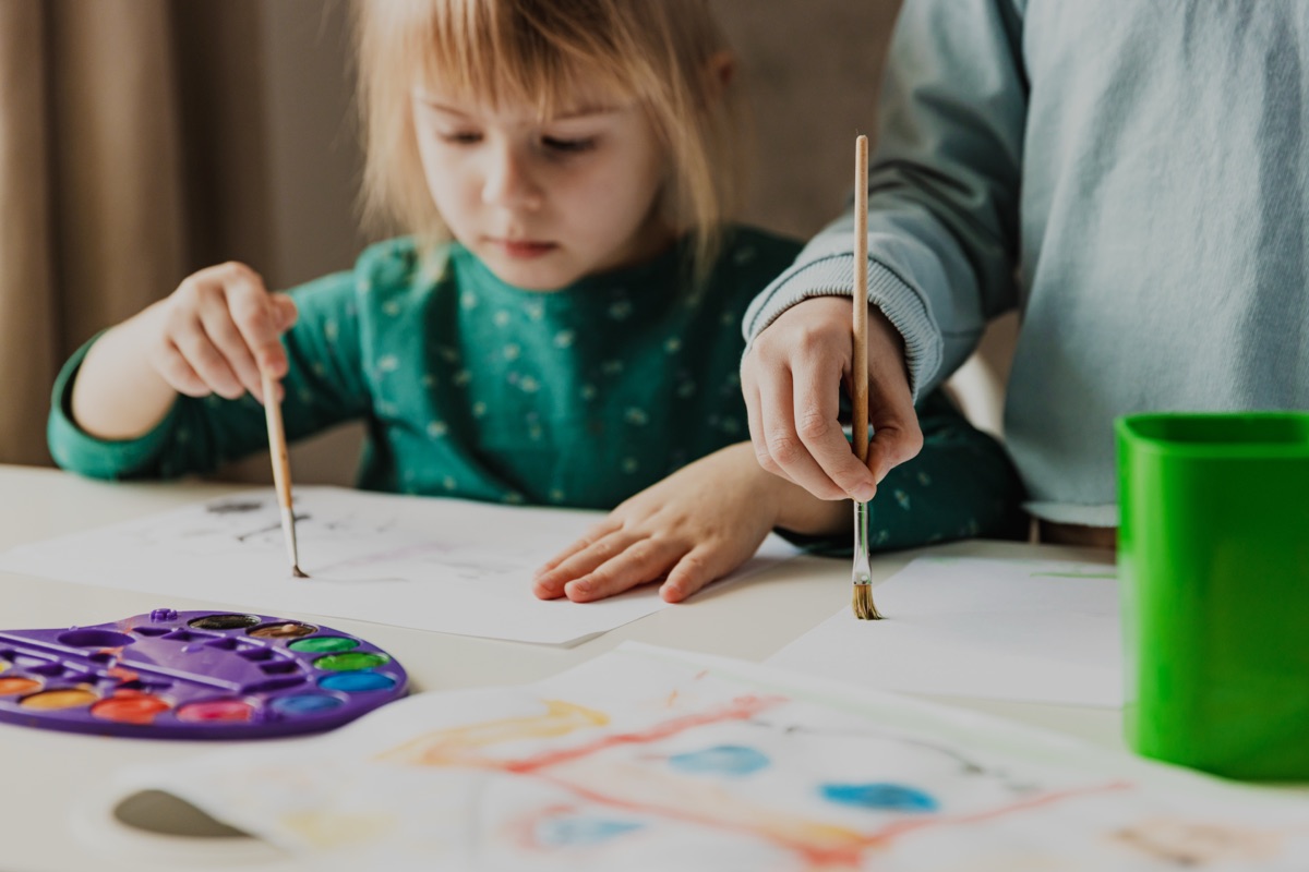 A pre-school child painting with watercolours beside an educator